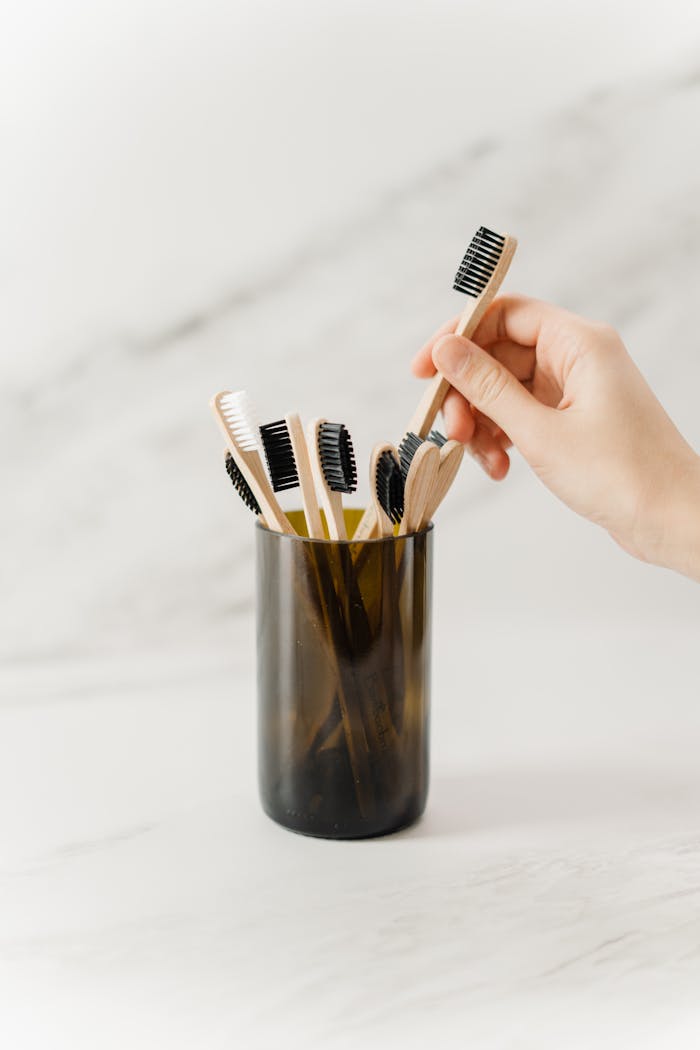 A hand selecting a wooden toothbrush from an eco-friendly collection in a holder.